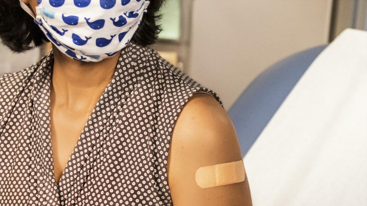 Person mit Mund-Nasen-Schutz und Pflaster auf dem Oberarm