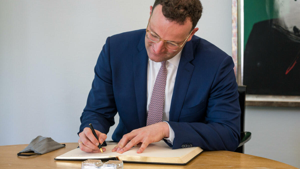 Jens Spahn sitzt an einem Tisch und schreibt in ein Buch.