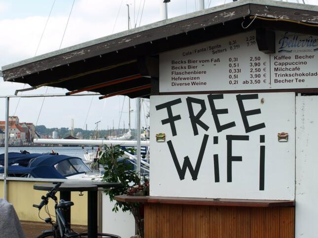 Eine kleine Kneipe in einer Holzhütte an einem Hafen. Die Hütte ist mit Brettern vernagelt. Auf einem steht Free WiFi.