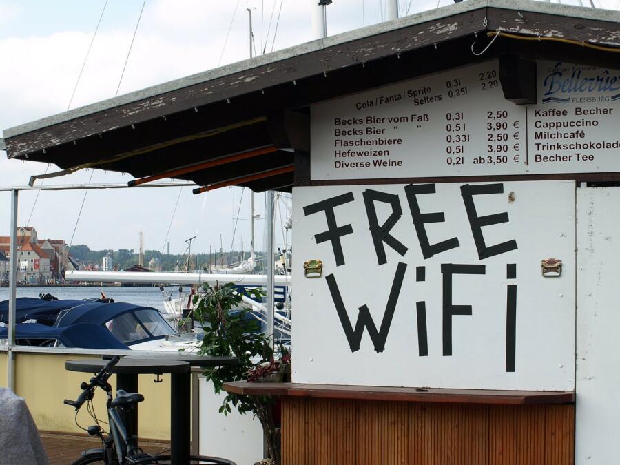 Eine kleine Kneipe in einer Holzhütte an einem Hafen. Die Hütte ist mit Brettern vernagelt. Auf einem steht Free WiFi.