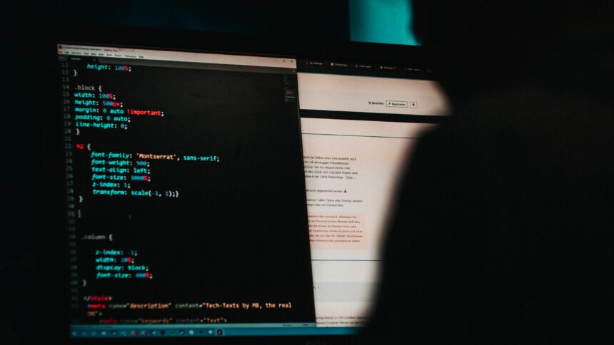 Eine Person sitzt in einem dunklen Raum vor einem Bildschirm und betrachtet einen HTML-Code.