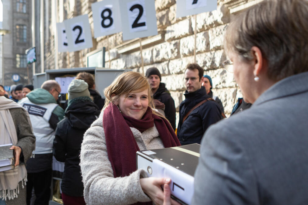 Eine Frau übergibt vor einem großen Gebäude in Berlin mehrere Aktenordner.