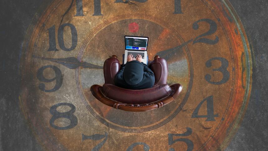 Mensch mit Laptop von oben fotografiert, der in einer auf den Boden gemalten Uhr sitzt