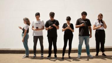 Sechs junge Menschen stehen in einer Reihe, alle schauen auf ihr Smartphone.