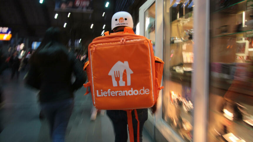 Eine Person mit großem, oragenen Lieferandorucksack im Frankfurter Hauptbahnhof