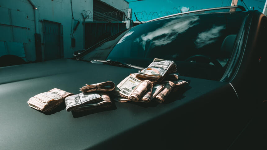 Geldbündel liegen auf der Haube eines schwarzen Autos.