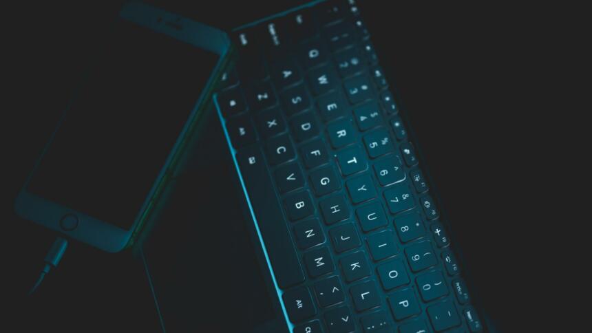 Dunkles Foto einer Tastatur mit beleuchteten Buchstaben und iPhone