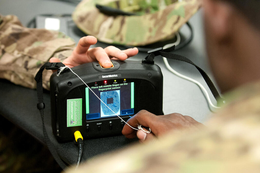 Das Bild zeigt einen Iris- und Fingerabdruckscanner in der Hand von US-Soldat:innen.