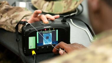 Das Bild zeigt einen Iris- und Fingerabdruckscanner in der Hand von US-Soldat:innen.