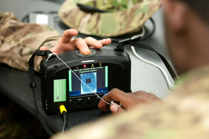 Das Bild zeigt einen Iris- und Fingerabdruckscanner in der Hand von US-Soldat:innen.