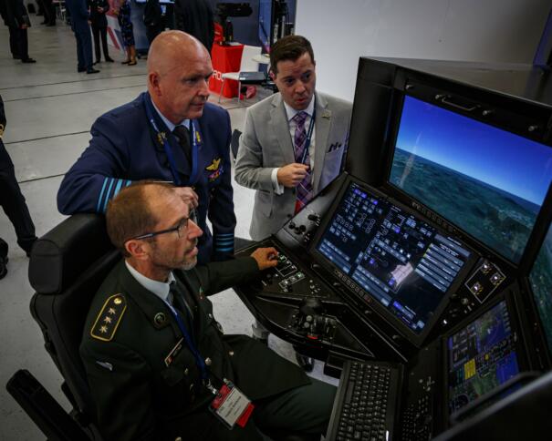 Das Bild zeigt drei Männer beim Steuern einer Drohne an Bildschirmen.