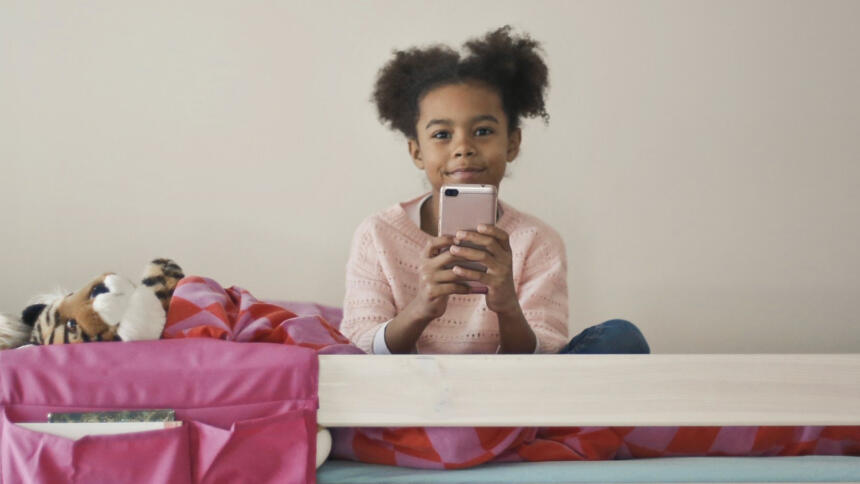 Ein Mädchen sitzt auf einem Bett und hält ein Handy.