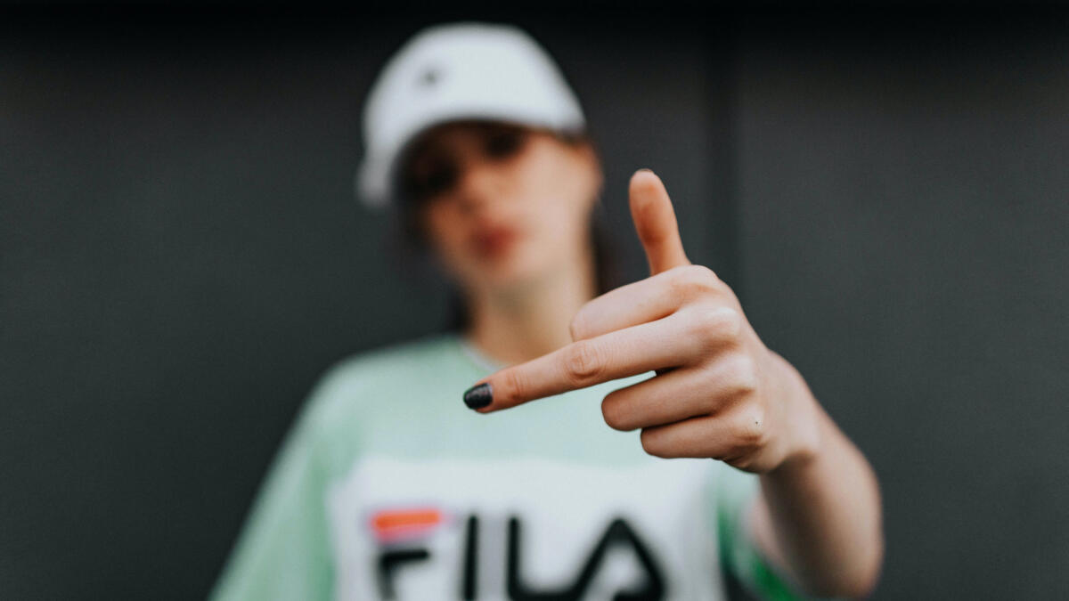 Eine Frau mit Kappe zeigt den Mittelfinger in die Kamera.