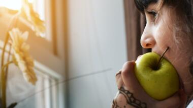 Eine Person beißt in einen Apfel und schaut aus dem Fenster