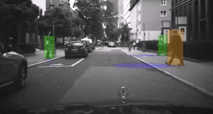 Kamerabild aus der Sicht eines Autofahrers, drei Fußgänger am Straßenrand, zwei bewegen sich Richtung Fahrbahn. Geometrische Formen zeigen an, welchen Aufenthaltsort die Software für die Fußgänger vorhersagt.