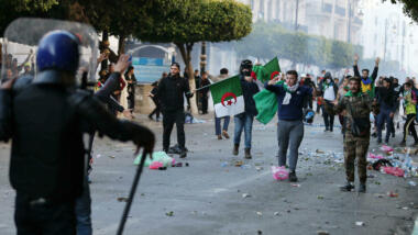 Demonstranten mit Algerienflaggen stehen behelmten Polizisten gegenüber