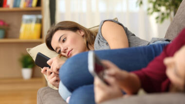 Jugendliches Mädchen liegt auf dem Sofa und guckt ernst auf ihr Smartphone