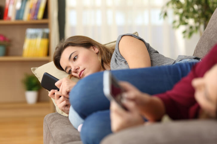 Jugendliches Mädchen liegt auf dem Sofa und guckt ernst auf ihr Smartphone