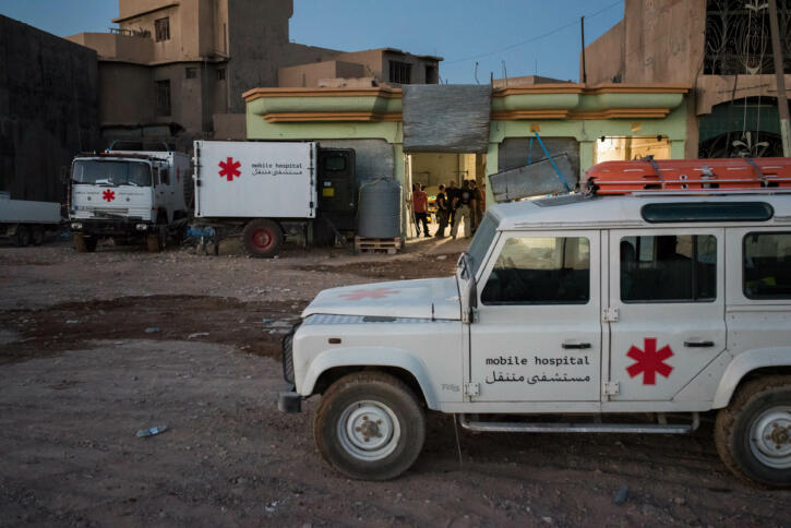 Autos und Anhänger mit der Aufschrift "mobile hospital" auf Englisch und Arabisch stehen in einer Stadt in der Wüste
