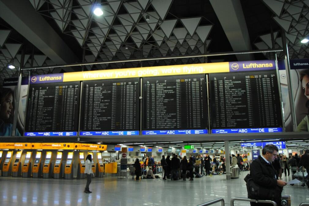 Das Bild zeigt die Anzeigetafel des Flughafens Frankfurt, eingerahmt von Werbung für Lufthansa.