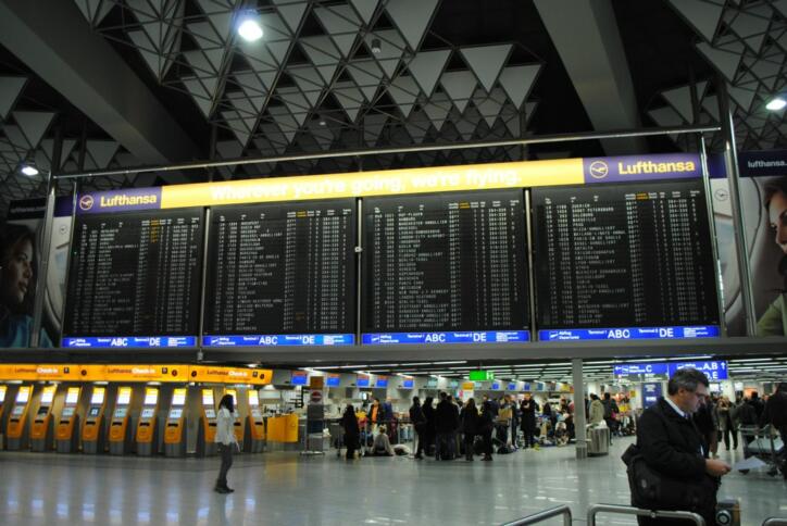 Das Bild zeigt die Anzeigetafel des Flughafens Frankfurt, eingerahmt von Werbung für Lufthansa.