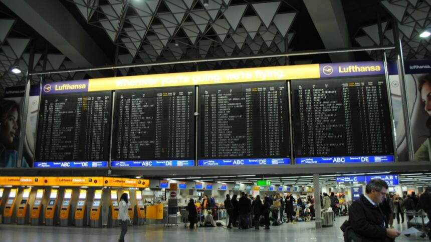 Das Bild zeigt die Anzeigetafel des Flughafens Frankfurt, eingerahmt von Werbung für Lufthansa.