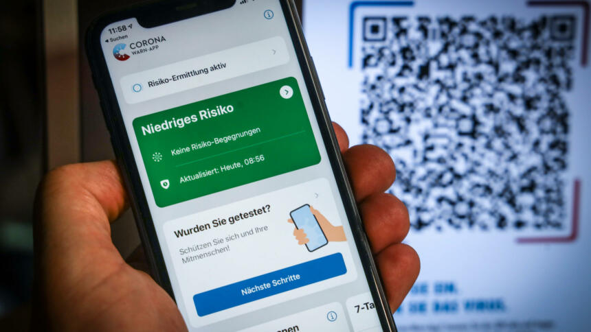 Smartphone, auf dem die Corona-Warn-App geöffnet ist. Im Hintergrund ein QR-Code für den Check-in mit der Corona-Warn-App.