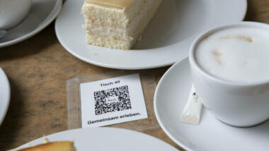 Luca-QR-Code zwischen Kaffeetassen und Kuchenstücken.