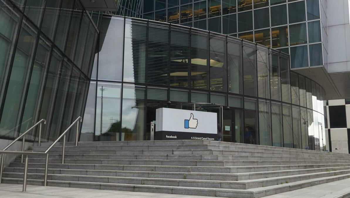 Betontreppen und gläserne Hausfront, davor ein Schild mit dem nach oben gereckten Facebook-Daumen