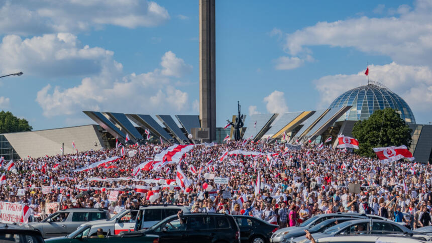 Das Bild zeigt Tausende Menschen auf einer Demonstration, sie tragen weiß-rote Banner.