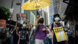 Menschen mit einen gelben Regenschirm und Protestplakaten auf einer Straße in Hongkong.