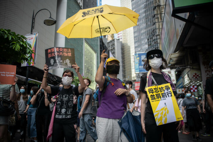Menschen mit einen gelben Regenschirm und Protestplakaten auf einer Straße in Hongkong.