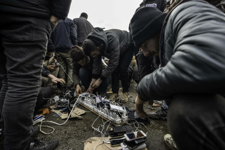 Das Bild zeigt einige Männer in WInterjacken, die um einen Mehrfachstecker mit Ladegeräten und damit verbundenen Handys sitzen.
