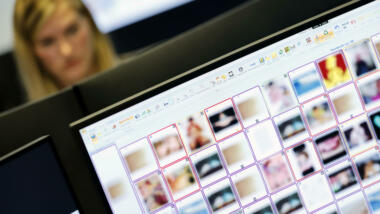 Ein Bildschirm mit verpixelten Bildern, im Hintergrund eine Mitarbeiterin der Hotline
