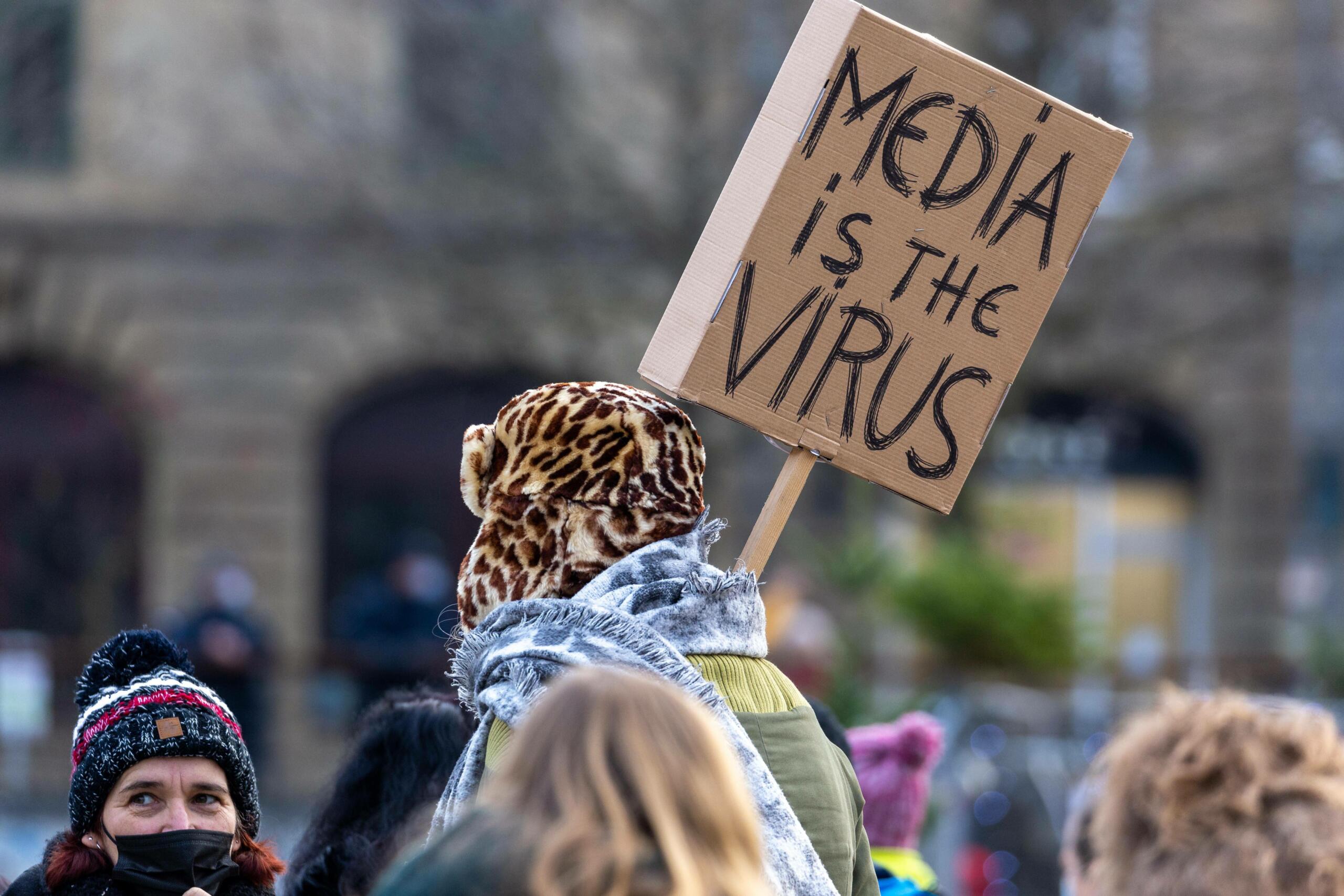 Eine Person auf einer Demo mit einem Schild: "Media is the Virus"