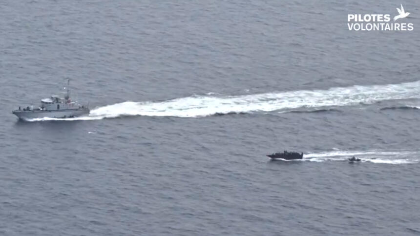 Das Bild zeigt ein Patrouillenboot der libyschen Küstenwache, das den Weg eines voll besetzten Schlauchbootes kreuzt, dem wiederum ein Schlauchboot der Küstenwache folgt.