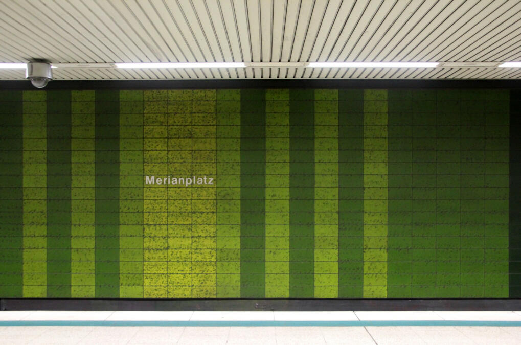 Das Bild zeigt einen Bahnsteig im U-Bahnhof, an der grün gekachelten Wand steht die Aufschrift "Merianplatz", an der Decke hängt eine Videokamera.