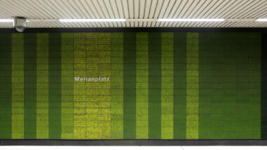 Das Bild zeigt einen Bahnsteig im U-Bahnhof, an der grün gekachelten Wand steht die Aufschrift "Merianplatz", an der Decke hängt eine Videokamera.