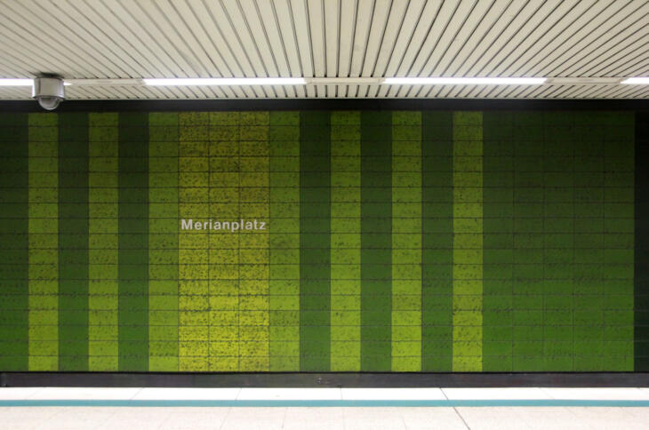 Das Bild zeigt einen Bahnsteig im U-Bahnhof, an der grün gekachelten Wand steht die Aufschrift "Merianplatz", an der Decke hängt eine Videokamera.