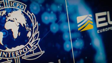Das Bild zeigt die Logos von Interpol und Europol vor dunkelblauem Hintergrund.