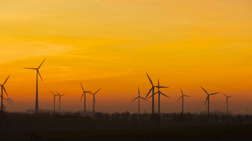 Mehrere Windräder vor einem vom Sonnenuntergang orangenen Himmel