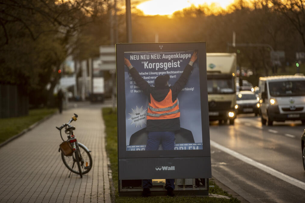 Mensch hängt Plakat in Plakatkasten auf