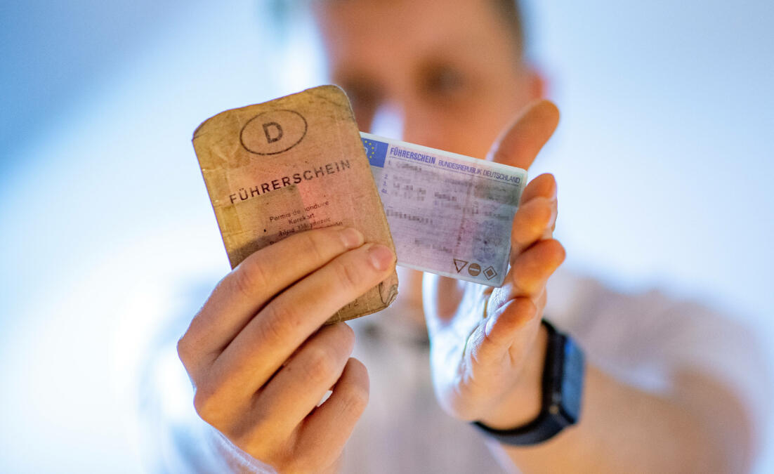 Verschwommen erscheinende Peroson, die einen alten papiernen und einen neuen Plastikführerschein hält