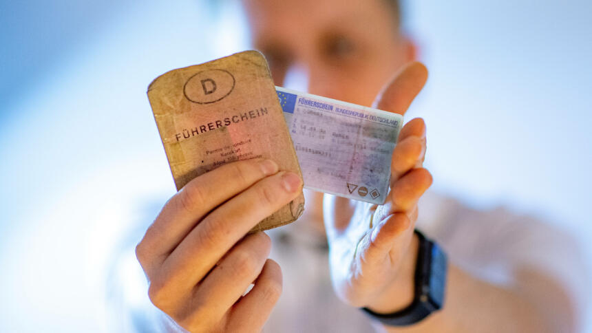 Verschwommen erscheinende Peroson, die einen alten papiernen und einen neuen Plastikführerschein hält