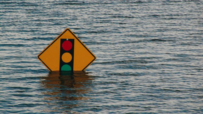 Ein gelbes Verkehrszeichen, auf dem eine Ampel abgebildet ist, steht aus dem Wasser.