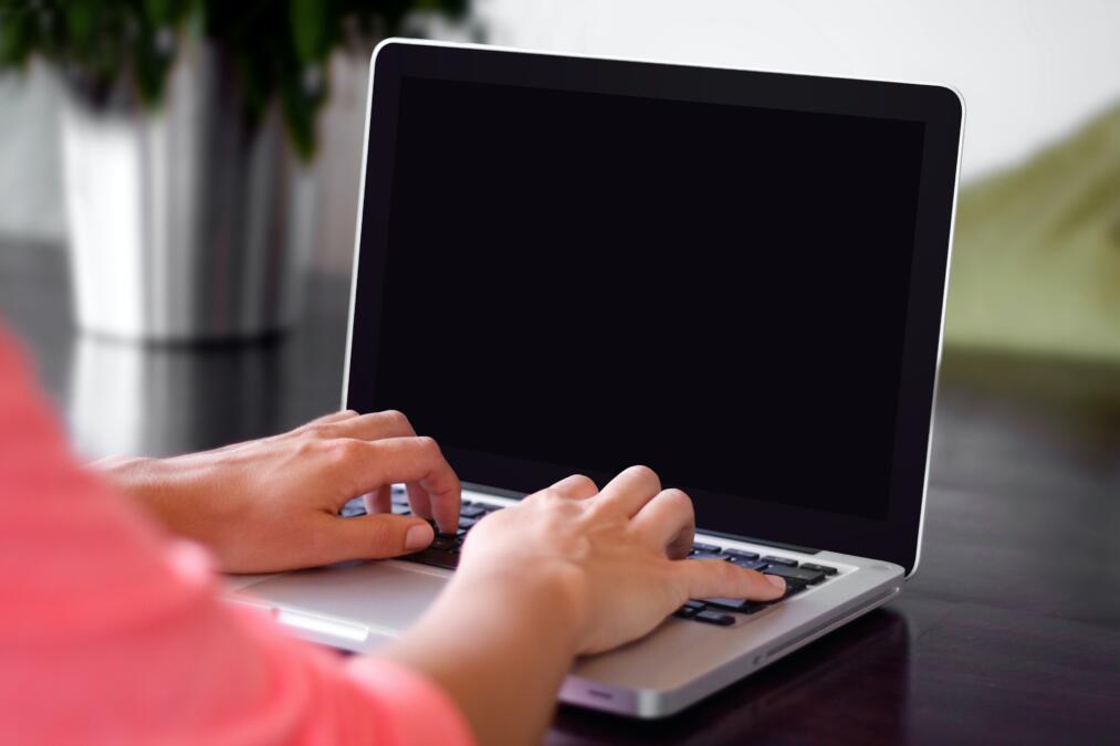 Ein Laptop mit schwarzem Bildschirm, auf der Tastatur liegen zwei Hände.