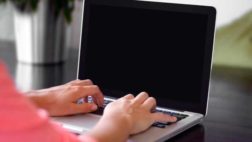 Ein Laptop mit schwarzem Bildschirm, auf der Tastatur liegen zwei Hände.
