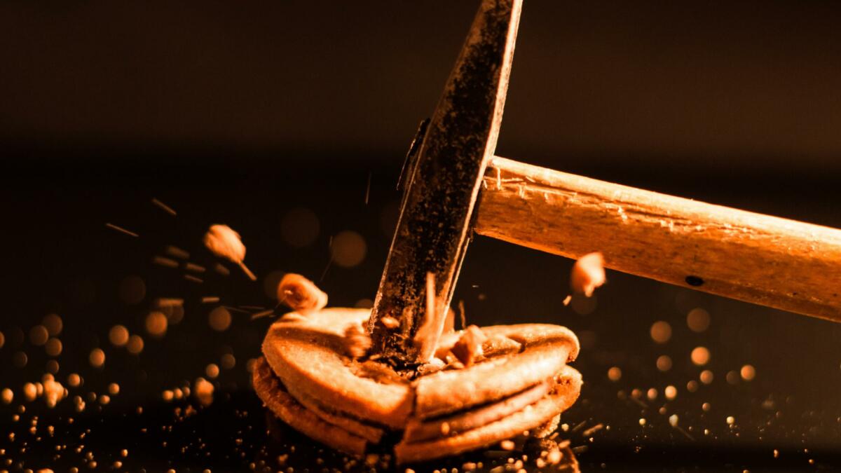 Nahaufnahme eines Kekses, der mit einem kleinen Hammer zerschlagen wird und in Einzelteile zersplittert