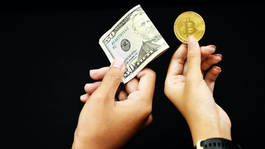 Zwei Hände ragen vor schwarzem Hintergrund in das Bild. Die rechte hält ein Bitcoin, die linke eine Geldschein.