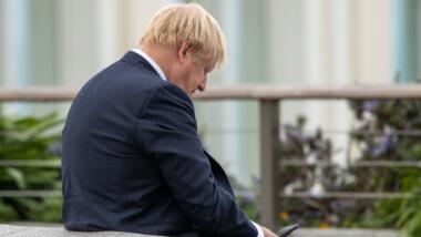 Boris Johnson lehnt sich an eine Mauer und schaut auf sein Smartphone